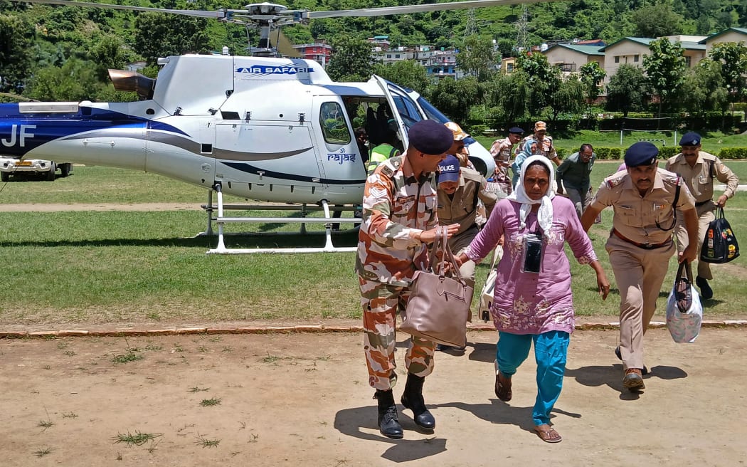 Indian security personnel escort people deboarding a helicopter after they were evacuated during a rescue operation, at the Indo-Tibetan Border Police (ITBP) camp in Uttarkashi district on August 7, 2025, two days after a cloudburst caused a massive mudslide and flash floods in India's Uttarakhand state. The Indian army brought in sniffer dogs, drones and heavy earth-moving equipment on to search for scores of people missing a day after deadly Himalayan flash floods. At least four people were killed and more than 50 are unaccounted for after a wall of muddy water and debris tore down a narrow mountain valley, smashing into the town of Dharali in Uttarakhand state, rescue officials said on August 6. (Photo by AFP)