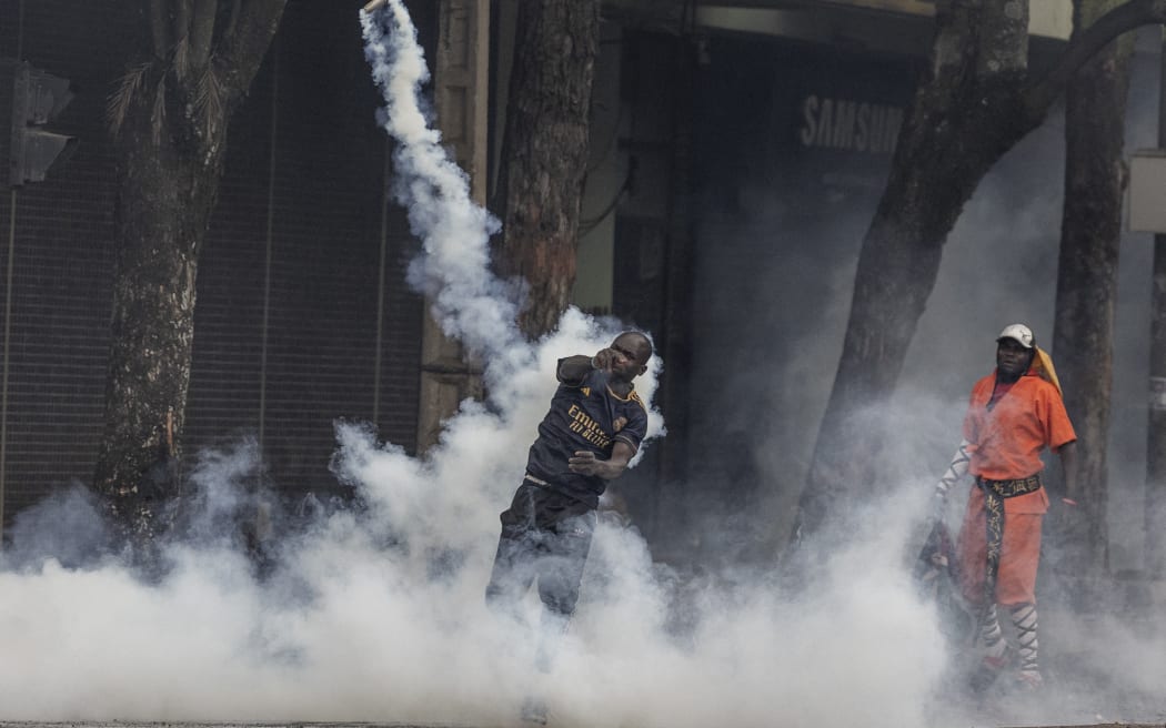 A protester hurls a teargas canister at Kenya police officers during clashes in downtown Nairobi on June 25, 2025 during a planned day of protest marking the first anniversary of the storming of the parliament. Marches in Kenya to mark a year since massive anti-government demos turned violent on Wednesday, with two killed and running battles between protesters and police, who flooded Nairobi's streets with tear gas and sealed off government buildings with barbed wire. (Photo by SIMON MAINA / AFP)