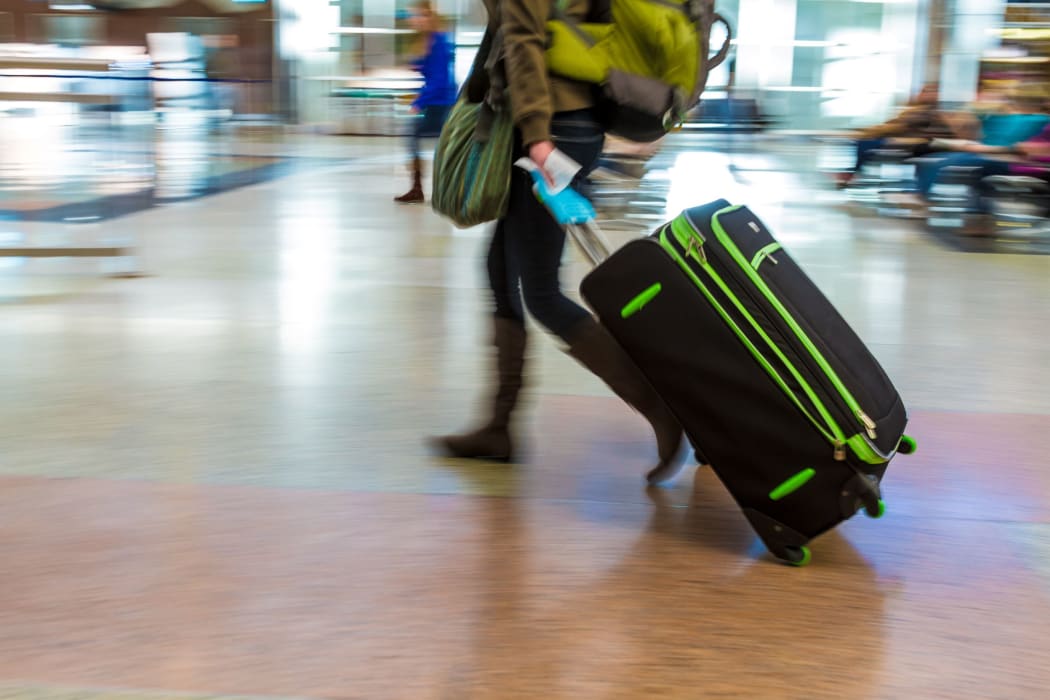 A woman with a backpack pulls a suitcase through an airport.
