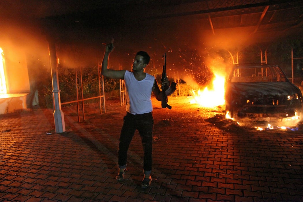 A file picture taken on September 11, 2012 shows an armed man waving his rifle as buildings and cars are engulfed in flames after being set on fire inside the US consulate compound in Benghazi.