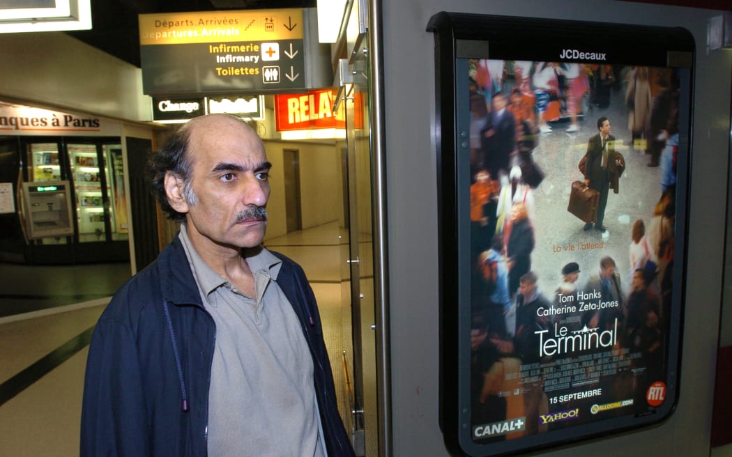 Mehran Karimi Nasseri passes by the poster of the movie inspired by his life 12 August 2004 in the terminal one of Paris Charles De Gaulle airport. Known as "Sir Alfred Mehran", Mehran Karimi Nasseri is a 59 year-old Iranian refugee who has been living in Roissy for 16 years, and whose life has therefore inspired American film director Steven Spielberg for the character of the protagonist in the movie "The Terminal".