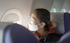 Passenger sitting in cabin of airplane wearing face mask looking out of window.