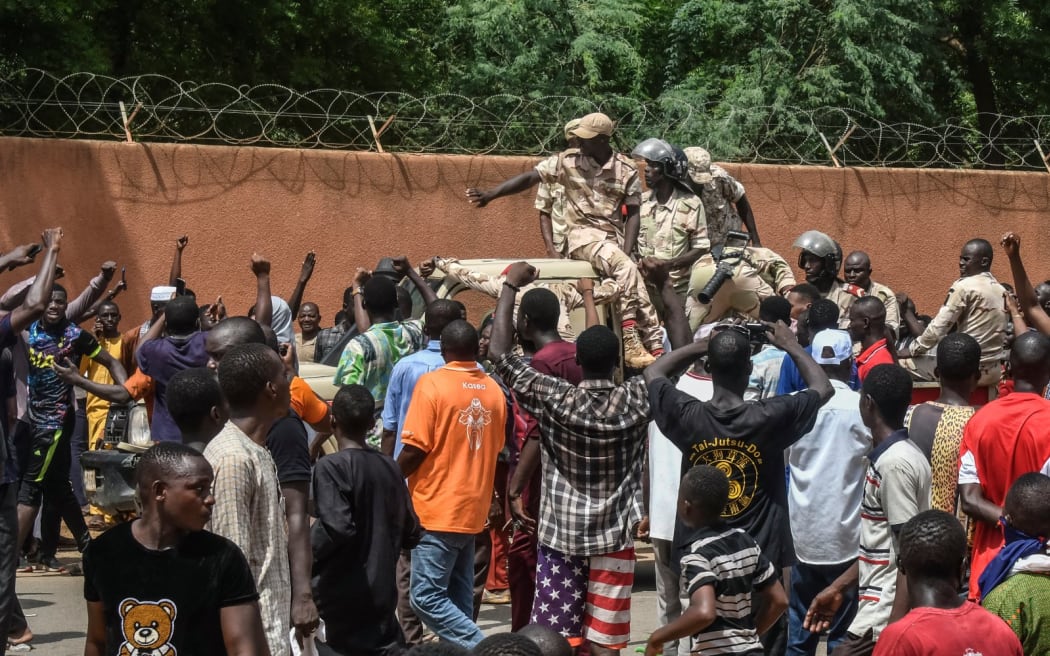 Protesters cheer Nigerien troops as they gather in front of the French Embassy in Niamey during a demonstration that followed a rally in support of Niger's junta in Niamey on July 30, 2023. Thousands of people demonstrated in front of the French embassy in Niamey on Sunday, before being dispersed by tear gas, during a rally in support of the military putschists who overthrew the elected president Mohamed Bazoum in Niger. Before the tear-gas canisters were fired, a few soldiers stood in front of the embassy to calm the demonstrators. (Photo by AFP)