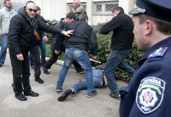 A police officer looks on as pro-Russian activists use a bat to beat a pro-Ukrainian supporter at the Sevastopol rally.