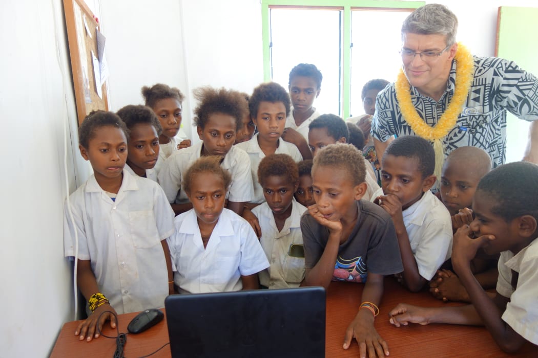 Students at Lambubu School crowd around the internet with Kacific's Jacques-Samuel Prolon.