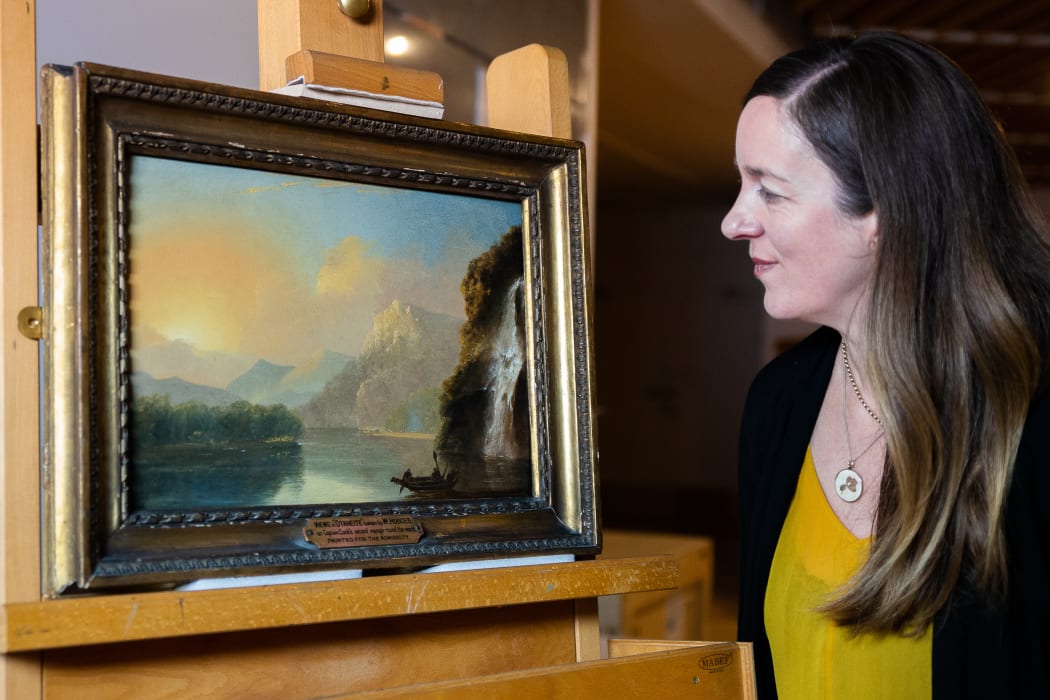 Curator of historical New Zealand art Rebecca Rice views Waterfall in Dusky Bay with Māori canoe.