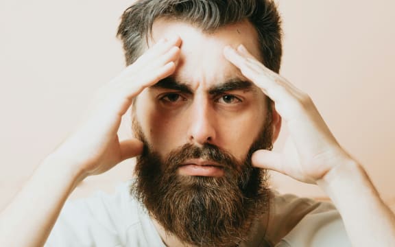 A bearded white man holds his hands to his head.
