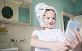 Girl looking at the smartphone screen and taking selfie at the bathroom.