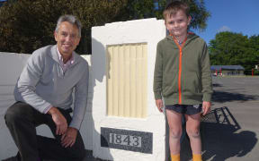 Principal Peter Verstappen with Kyro David Peter Baigent stand beside the sign which marks the opening year of Wakefield School.