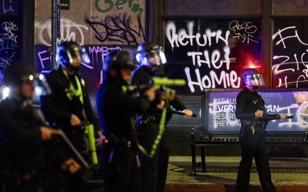 A graffiti reads “Return the Homies” behind Los Angeles police officers deployed next to City Hall as clashes with protesters continue into the night during a protest following federal immigration operations, in Los Angeles, California on June 8, 2025. Demonstrators torched cars and scuffled with security forces in Los Angeles on June 8, as police kept protestors away from the National Guard troops President Donald Trump sent to the streets of the second biggest US city. (Photo by ETIENNE LAURENT / AFP)