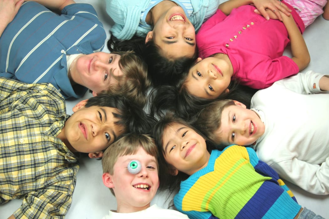 A photo of seven mixed race children all lying with their heads in a circle