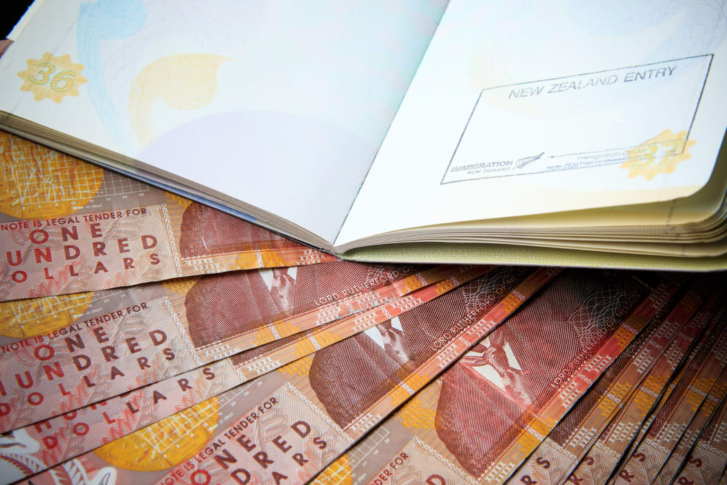 one hundred new zealand cash money bank note on table with red cover passport book