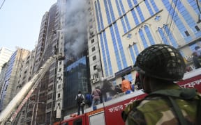 A Bangladehi Army stnad guard as Bangladeshi firefighters on ladders work to extinguish a blaze in Dhaka.