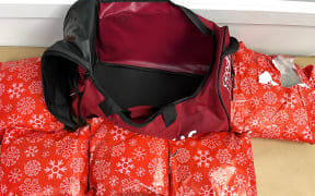 A red duffle bag is sitting on top of a number of what appears to be wrapped Christmas gifts in red paper with snowflakes on it.