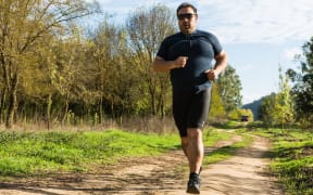 67035726 - big belly man jogging , exercising, doing cardio in the park , slightly overweight, loosing weight. on a lawn of green grass between trees without leaves.