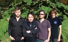 The Chills band members standing in front of a plant