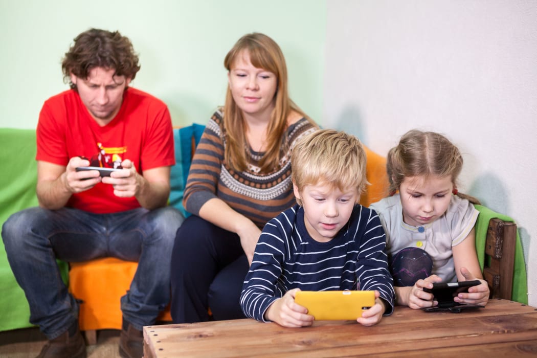36913913 - children and husband are passionate about games in the phone, mother looking at the kids