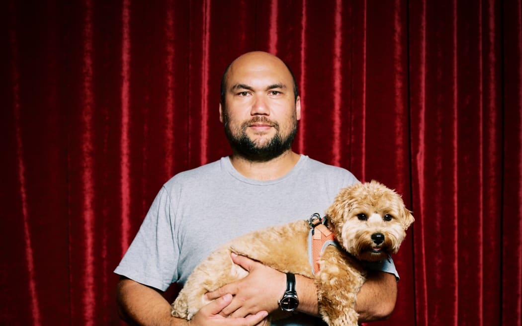 Casually dressed man holding a cute West Highland terrier dog in front of a red velvet curtain