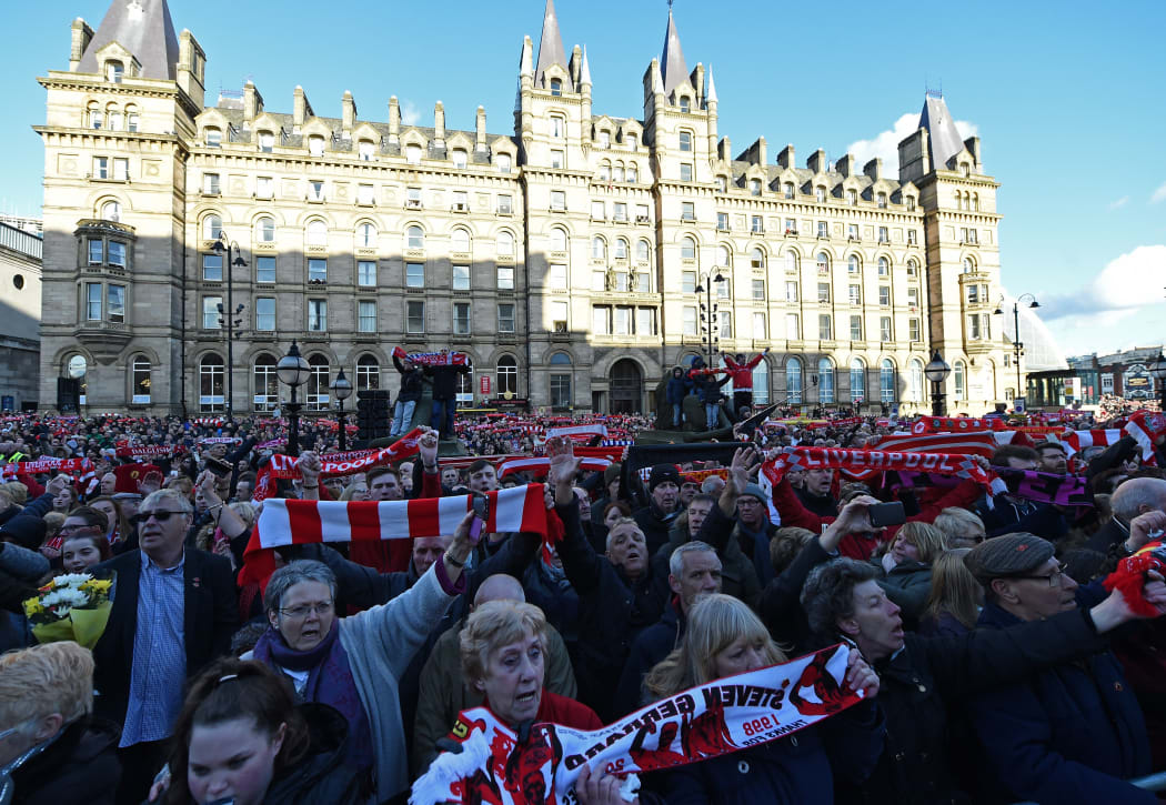 People hold Liverpool football scarves in the air as they sing "You'll Never Walk Alone" outside St George's Hall in Liverpool.