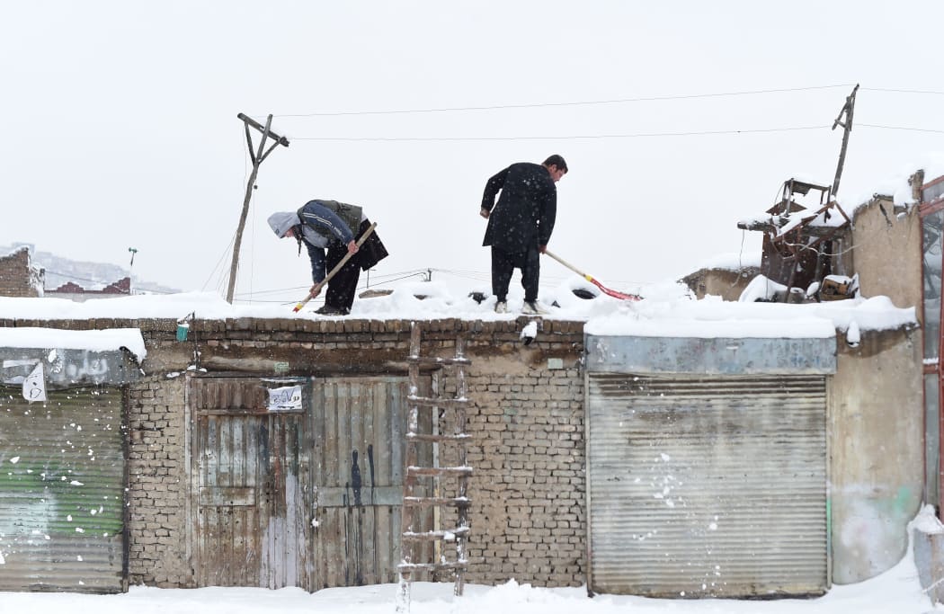 Afghan shopkeepers shovel snow from the roof of their shop during snowfall in Kabul on February 5, 2017.