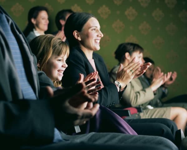 Parent and child clapping among audience who are watching performance.