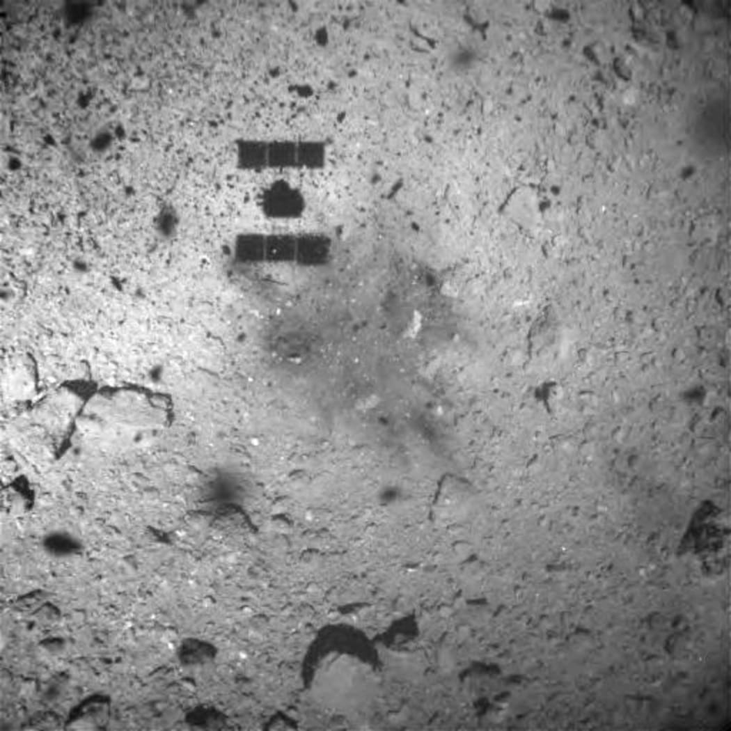 The image taken from on board Japan's Hayabusa-2 spacecraft shows the shadow of Hayabusa2 and a region of the surface that seems to have been discoloured by the touchdown.