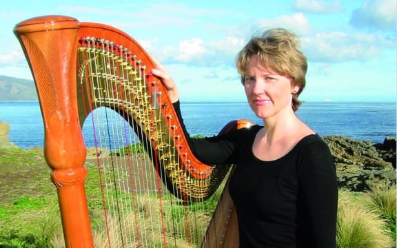 NZSO harpist Carolyn Mills stands beside her harp, with Wellington's south coast in the background.