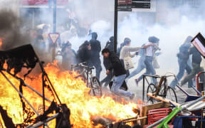 Protesters run in tear gas smoke next to   a street fire on the sidelines of a demonstration as part of a national day of strikes and protests, a week after the French government pushed a pensions reform through parliament without a vote, using the article 49.3 of the constitution, in Toulouse, southern France, on March 23, 2023. - French unions on March 23 staged a new day of disruption against the president's pension reform after he defiantly vowed to implement the change, which includes raising the age of retirement from 62 to 64, saying he was prepared to accept unpopularity in the face of sometimes violent protests. (Photo by Charly TRIBALLEAU / AFP)