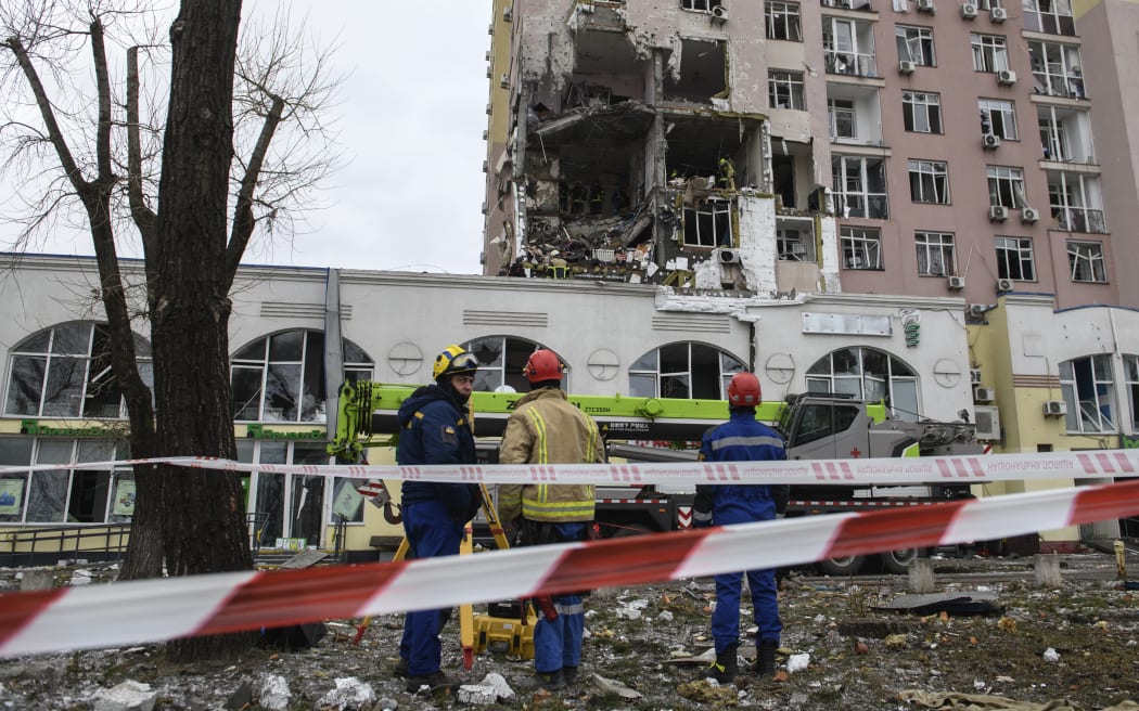 Ukrainian rescuers stand in front of a damaged residential building following Russian drones and missiles attack in Kyiv, on December 27, 2025, amid the Russian invasion in Ukraine. Russia pummelled Ukraine's capital with drones and missiles on December 27, killing a woman and cutting power to hundreds of thousands, ahead of the latest talks between the presidents of Ukraine and the US. (Photo by VLADYSLAV MUSIENKO / AFP)