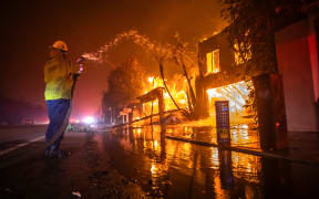 LOS ANGELES, CALIFORNIA - JANUARY 8: A firefighter battles the Palisades Fire while it burns homes at Pacific Coast Highway amid a powerful windstorm on January 8, 2025 in Los Angeles, California.  The fast-moving wildfire has grown to more than 2900-acres and is threatening homes in the coastal neighborhood amid intense Santa Ana Winds and dry conditions in Southern California. (Photo by Apu Gomes/Getty Images)