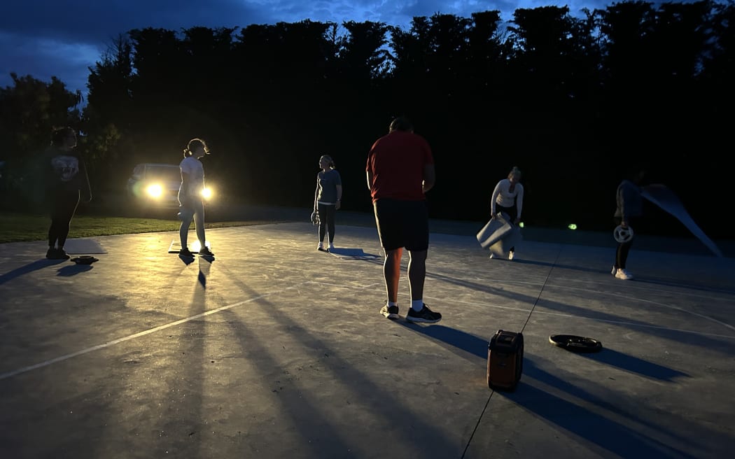 Photo of people working out in the dark, with a ray of car headlights providing some visibility.