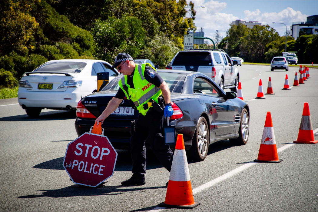 A Queensland police officer moves a stop sign at a vehicle checkpoint on the Pacific Highway, along the state's border with New South Wales, in Brisbane on April 15, 2020.