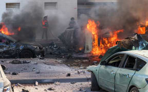 People try to extinguish fire on cars following a rocket attack from the Gaza Strip in Ashkelon, southern Israel, on October 7, 2023. Palestinian militant group Hamas has launched a "war" against Israel, Defence Minister Yoav Gallant said, after barrages of rockets were fired from the Gaza Strip into Israeli territory on October 7. (Photo by AHMAD GHARABLI / AFP)
