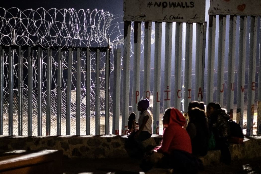 Migrants from Guatemala, part of the Central American migrant caravan, are seen near the US-Mexico border fence in Mexico on December 9, 2018. -