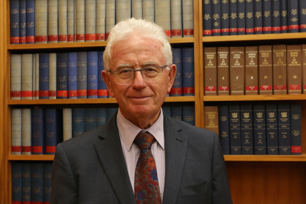 Sir Michael Cullen poses in the Labour Caucus Room in front of a bookcase of Hansard's verbatim reports of Parliament.