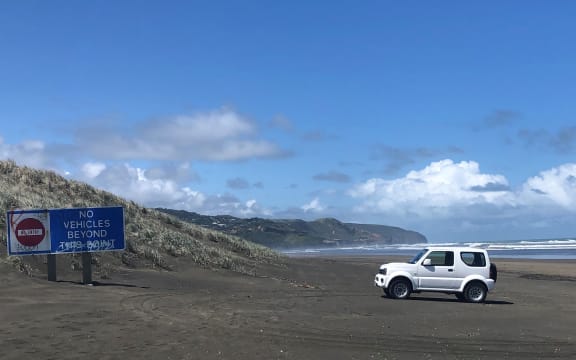 A white four-wheel driving is parked near a sign saying 'no vehicles beyond this point' on Muriwai Beach