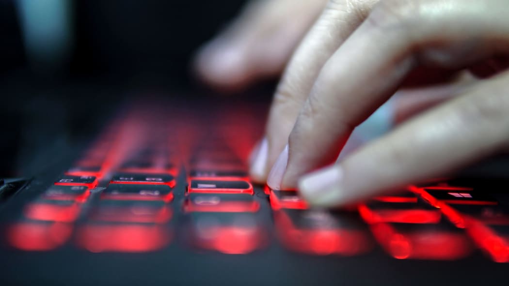Teenage Hacker Girl Attacks Corporate Servers in Dark, Typing on Red Lit Laptop Keyboard. Room is Dark
