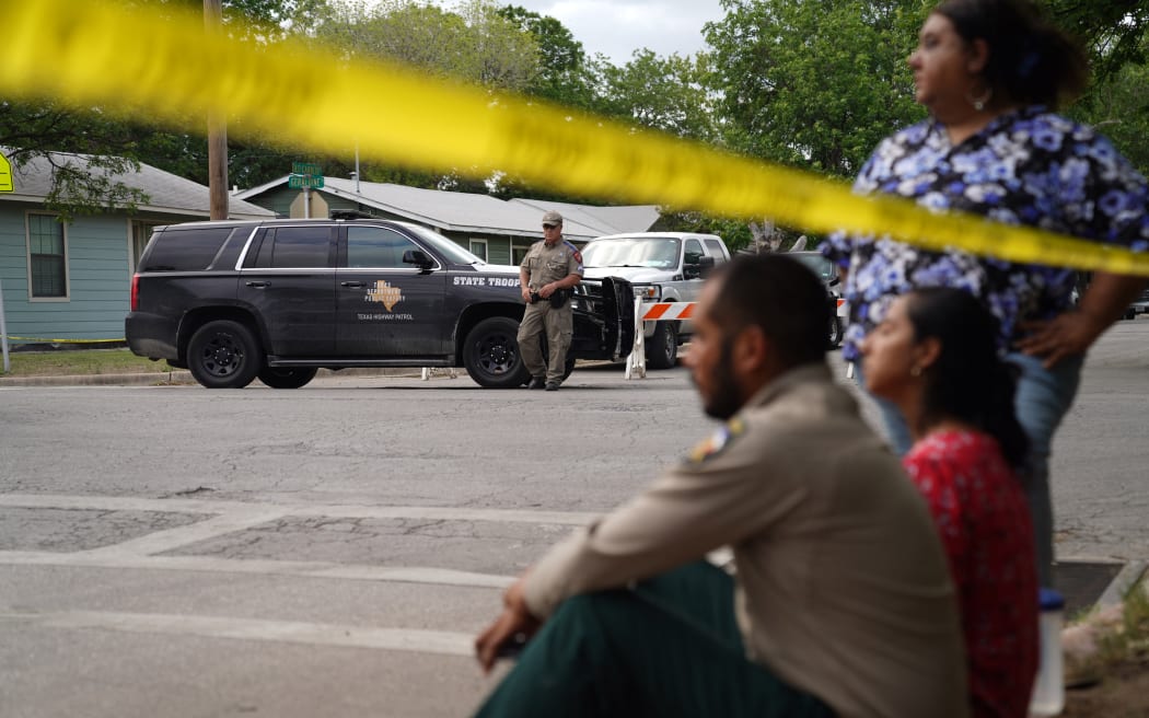 People sit on the curb outside of Robb Elementary School as State troopers guard the area in Uvalde, Texas.