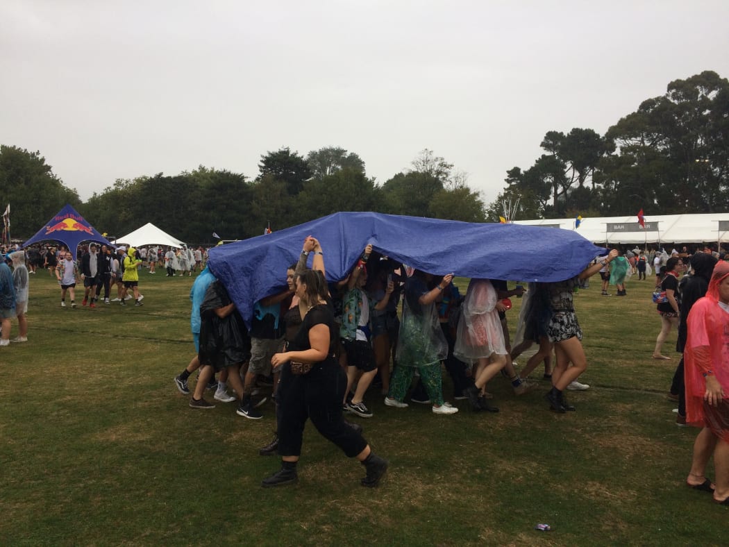 Punters at Christchurch's Electric Avenue festival use a tarp to keep back the rain