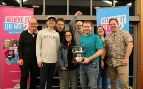 The champion quiz team “Eddie’s Back, Don’t Panic!” with team captain Kelvin Lange holding the trophy.