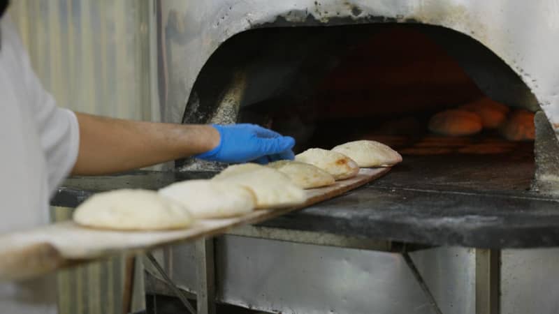 Fresh round bread being pulled out of wood fire oven at Zeki's Bakery.