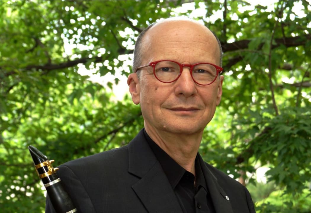 Clarinettist James Campbell with his clarinet in front of green tree foliage