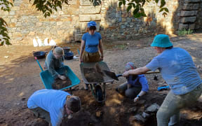 A group of people wearing sunhats and bandanas gathered around a dirt pit with shovels and wheelbarrows.