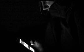 Hoody wearing young person peruses phone in the dark