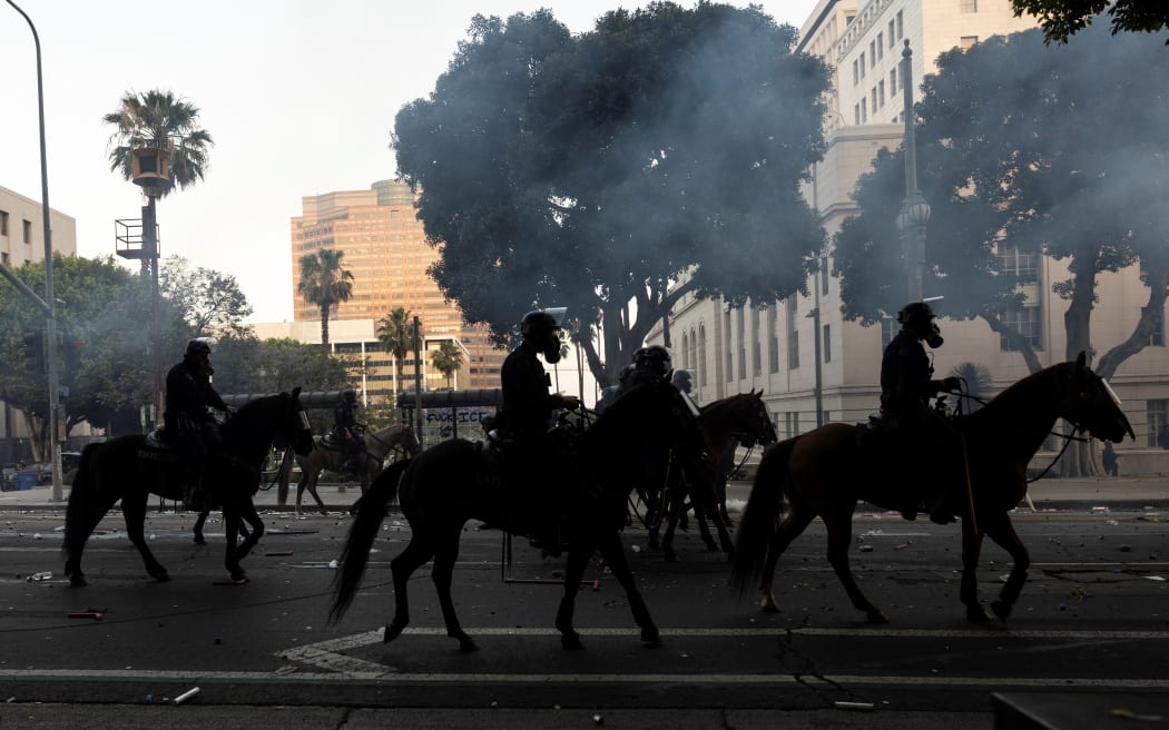 Los Angeles mounted police advance on a makeshift barricade in a cloud of tear gas as clashes erupt with demonstrators next to City Hall.