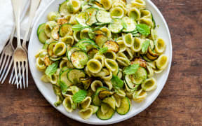 A large plateful of orecchiette with almond-mint pesto and garlic fried courgettes on a wooden board.