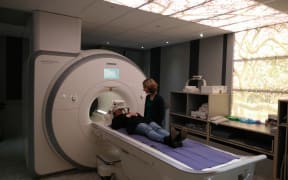 Senior Lecturer Dr Catherine Theys of the University of Canterbury stands next to a study participant in an fMRI scanner.