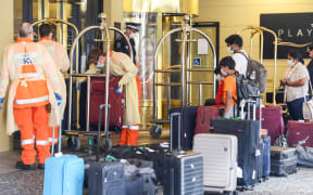 Local officials in protective gear help with baggage as Australian residents arrive at a hotel in Adelaide for mandatory 14-day quarantine after returning on a repatriation flight on 21 April 2020.