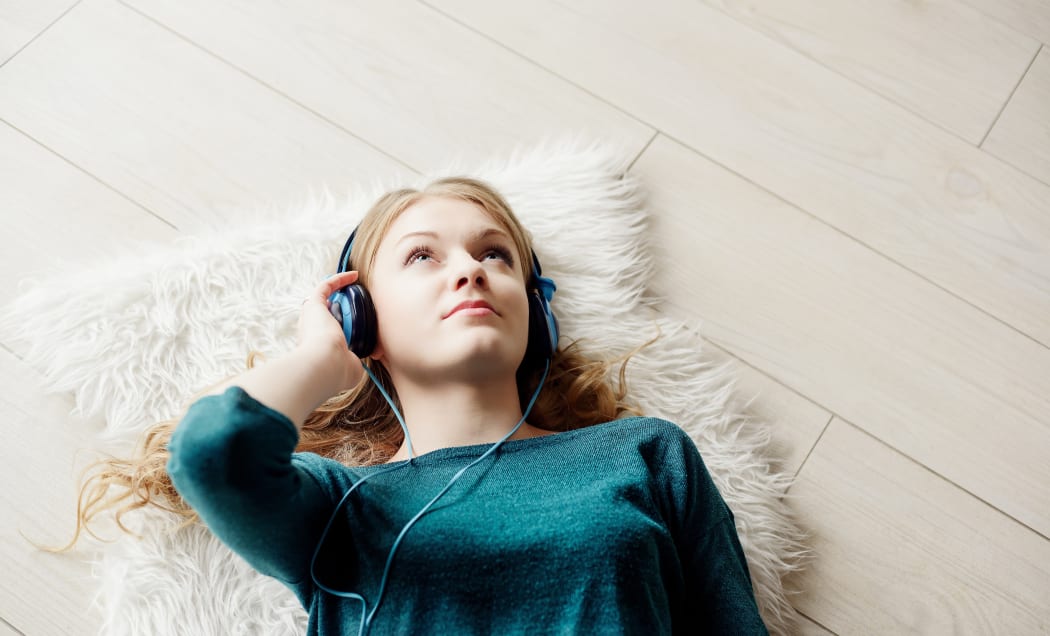 Beautiful blond woman listening to music through headphones. Lying on a wooden floor.