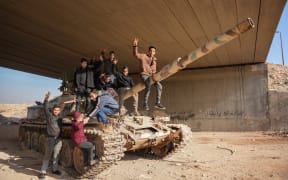 Syrians sit on an abandoned government tank in front of a slogan that reads "We are your men, Bashar" and "Long Live Syria", in the Damascus suburb of Daraya.
